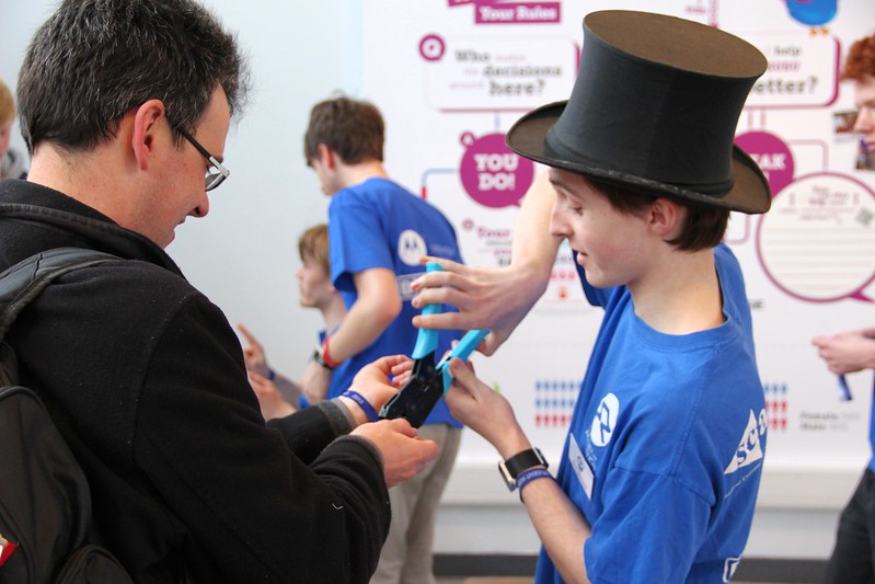 A blue shirted volunteer crimps a wristband onto a competition visitor