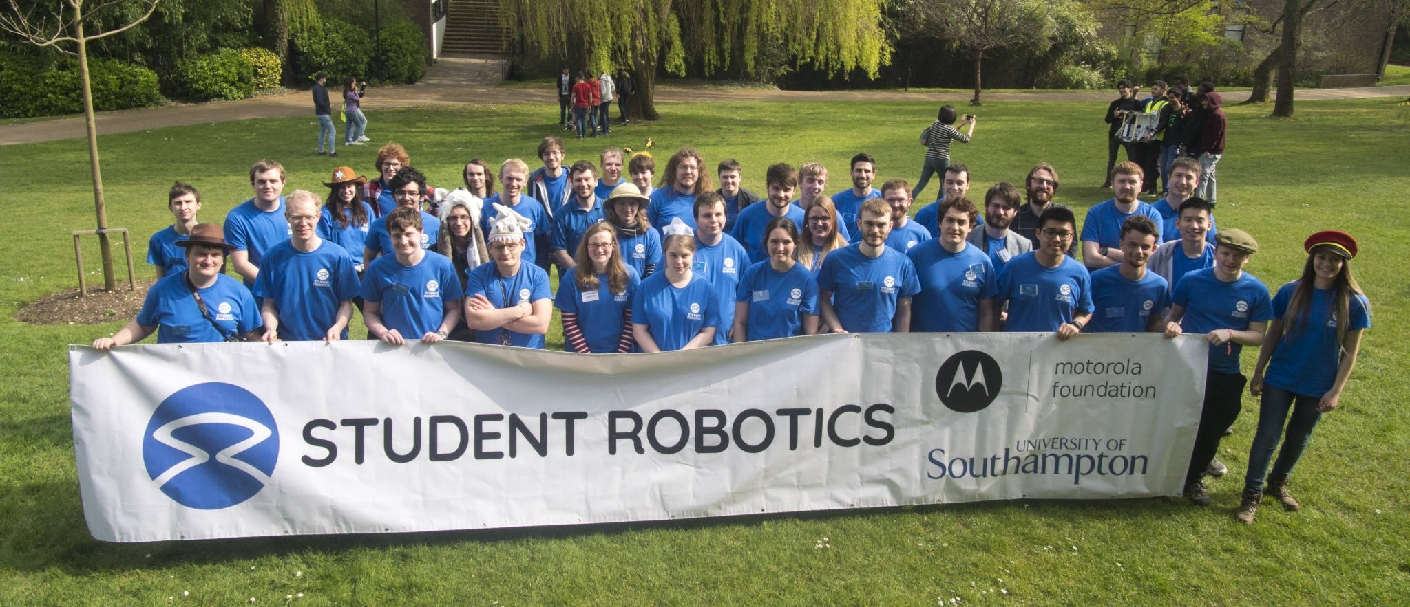 Group of around 50 blue shirted volunteers stood behind Student Robotics banner