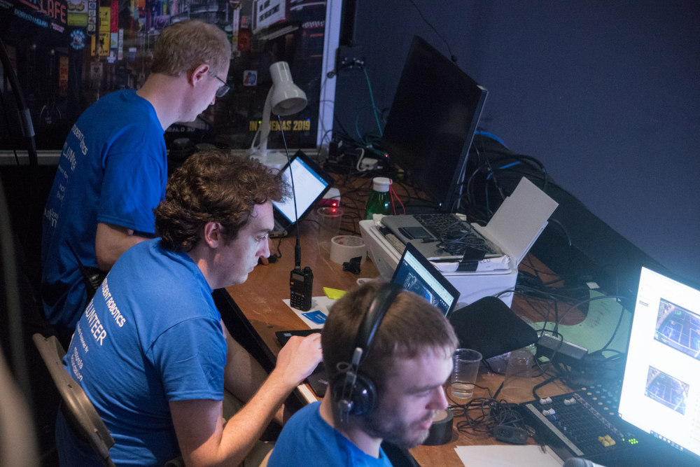 Three volunteers focused on their laptops which show livestreaming to YouTube